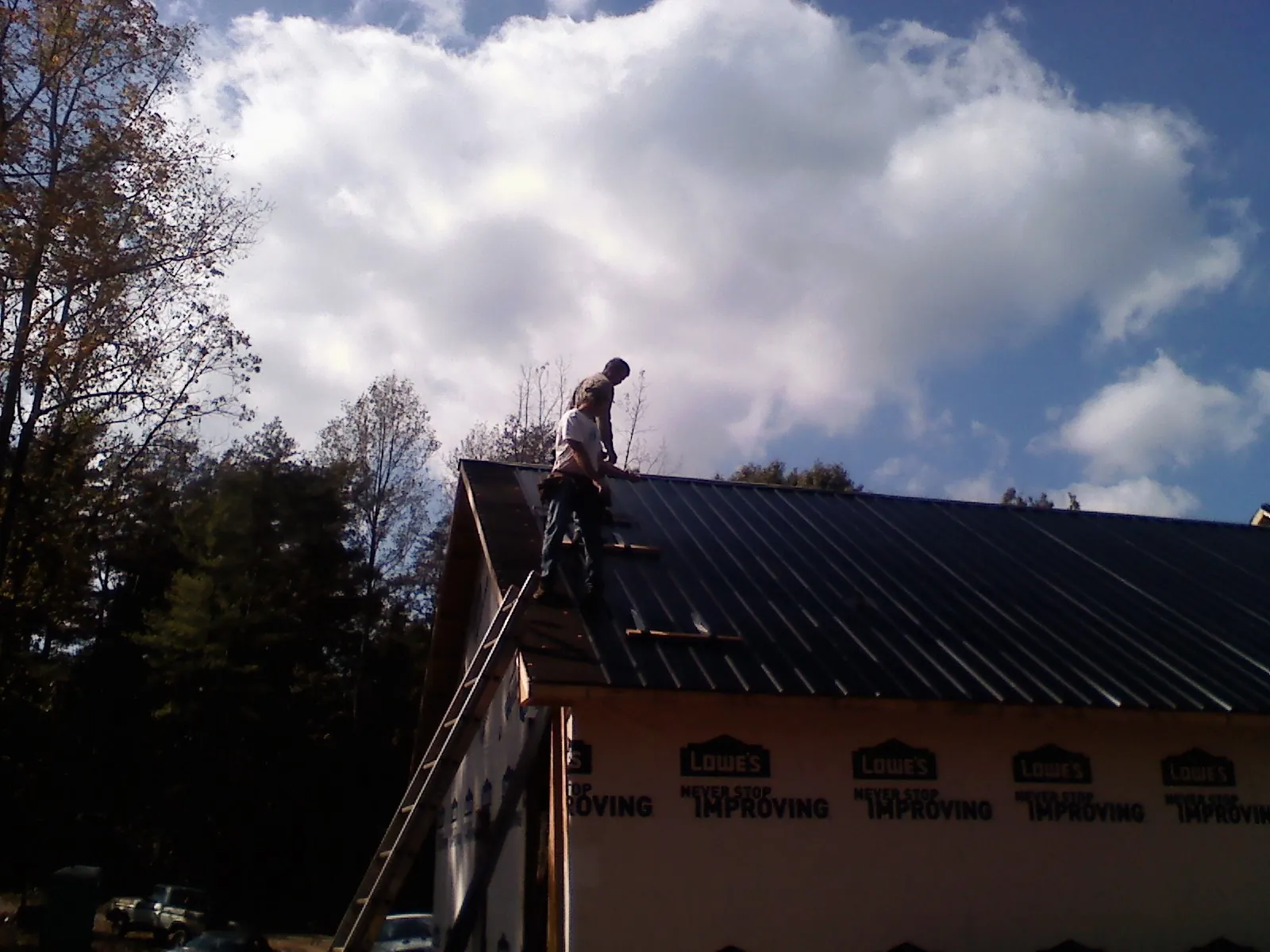 Roofer fastening dark metal panels high against a cloudy sky, from a Roof Inspection job in Wilbur
